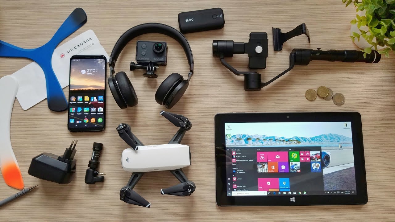 Collection of electronic devices including a smartphone, tablet, drone, and camera on a wooden surface.